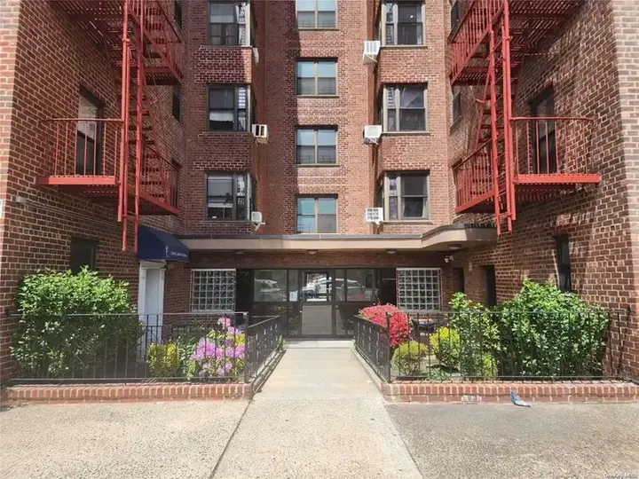 Red brick six-story apartment building with fire escapes, typical of Elmhurst, Queens