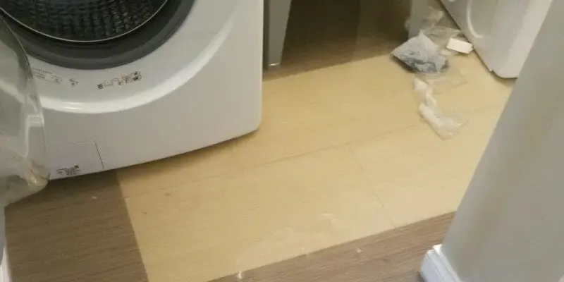Water on the floor beside a front-load washer after a hose leak in an Elmhurst apartment