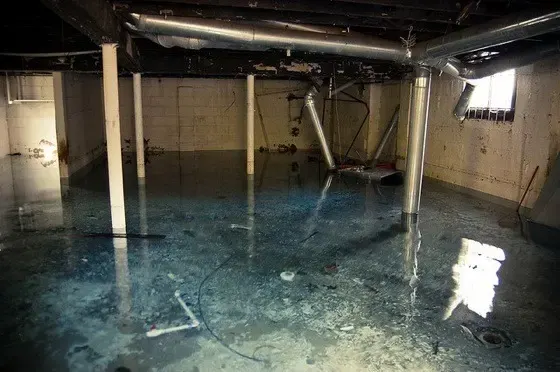 Standing water across an unfinished cellar with lally columns and ductwork in Elmhurst, Queens