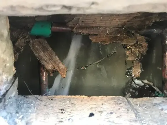 Copper supply pipe spraying water inside an opened plaster wall in an Elmhurst home