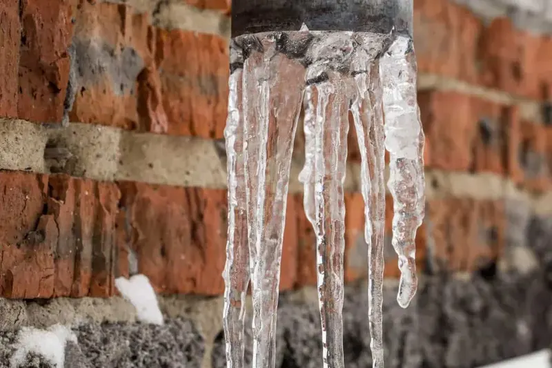 Icicles hanging from a frozen pipe against an old brick wall during a Queens cold snap