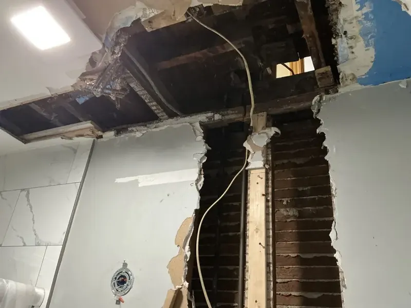 Opened wall chase exposing the pipe riser and ceiling joists in a Queens apartment building