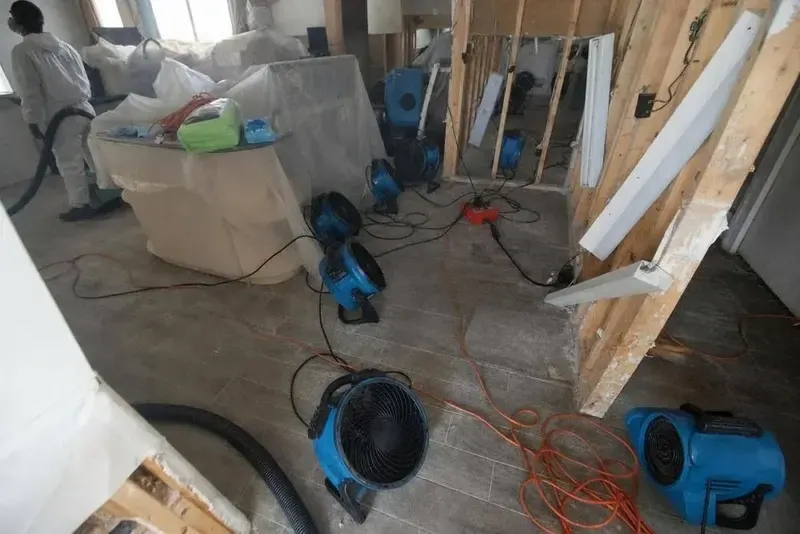 Air movers drying opened wall framing and subfloor during a structural dry-out in Queens
