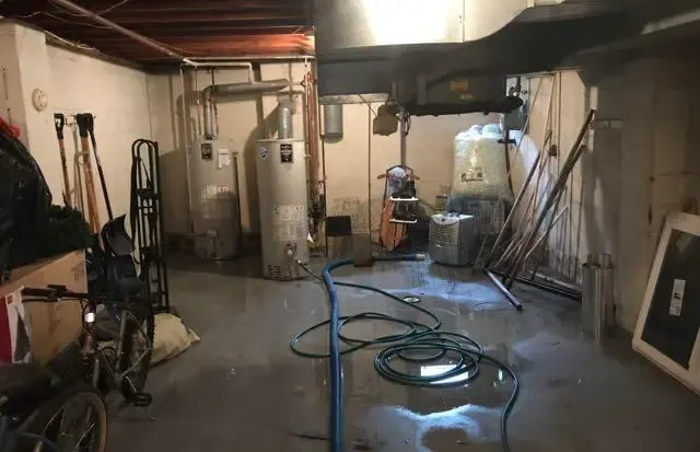 Water across a Queens cellar floor around two water heaters with an extraction hose